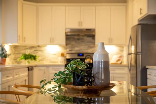 kitchen with stove, white cabinets, stainless steel refrigerator, and decorative backsplash