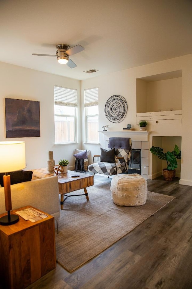 living room with ceiling fan, dark hardwood / wood-style flooring, and a tiled fireplace