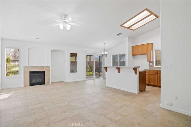 unfurnished living room featuring ceiling fan with notable chandelier, a tiled fireplace, vaulted ceiling, and a wealth of natural light