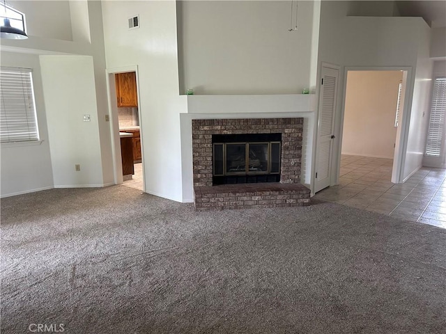 unfurnished living room featuring a high ceiling, visible vents, tile patterned flooring, and carpet
