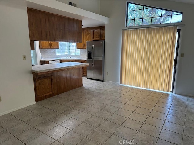 kitchen with decorative backsplash, tile counters, a peninsula, a sink, and stainless steel fridge with ice dispenser