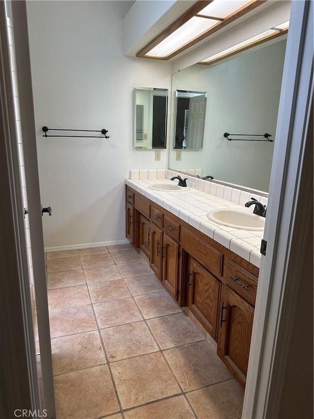 full bathroom with baseboards, double vanity, a sink, and tile patterned flooring