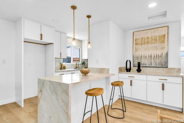 kitchen featuring white cabinetry, decorative light fixtures, light hardwood / wood-style floors, and kitchen peninsula