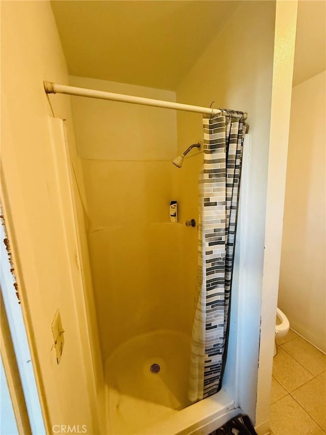 bathroom with a stall shower, toilet, and tile patterned floors