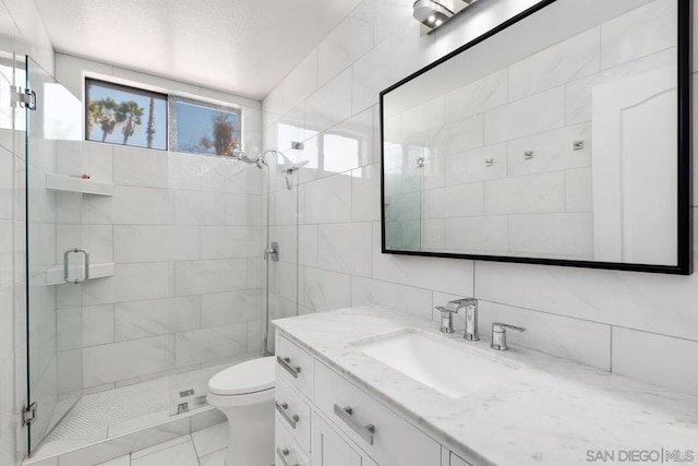 bathroom featuring a shower with door, vanity, tile walls, and toilet