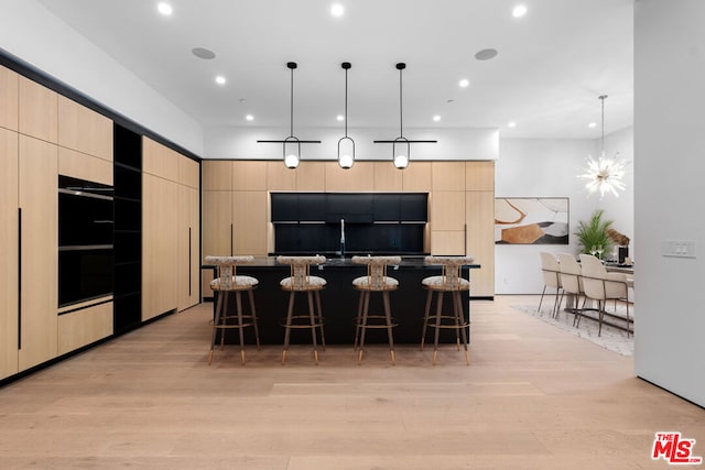 kitchen with a kitchen bar, light brown cabinetry, hanging light fixtures, a kitchen island, and light hardwood / wood-style floors