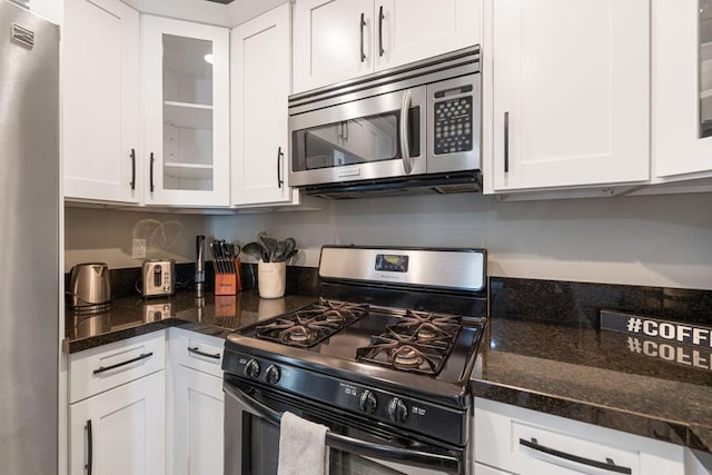 kitchen with stainless steel appliances, dark stone counters, and white cabinets