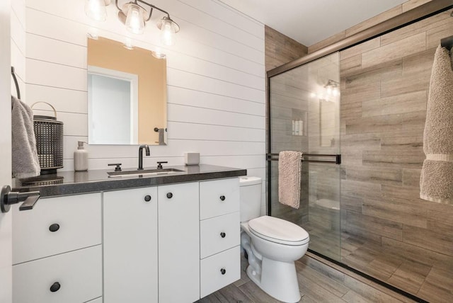 bathroom featuring wooden walls, wood-type flooring, vanity, walk in shower, and toilet