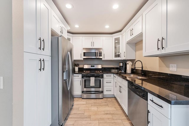 kitchen with white cabinetry, sink, stainless steel appliances, and dark stone countertops