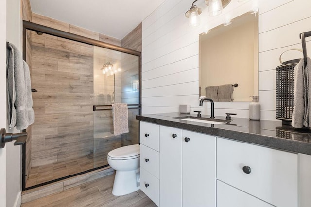 bathroom featuring wooden walls, wood-type flooring, vanity, toilet, and a shower with door