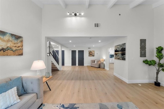 living room featuring beamed ceiling, a towering ceiling, and light hardwood / wood-style flooring