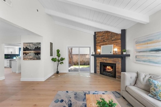 living room featuring a stone fireplace, light hardwood / wood-style flooring, and vaulted ceiling with beams