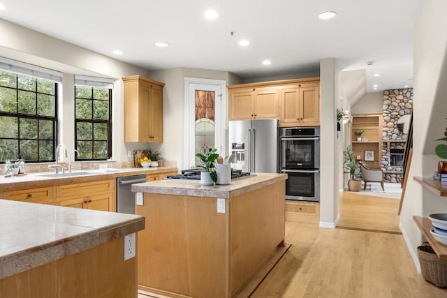 kitchen featuring sink, stainless steel appliances, a center island, light brown cabinetry, and light wood-type flooring