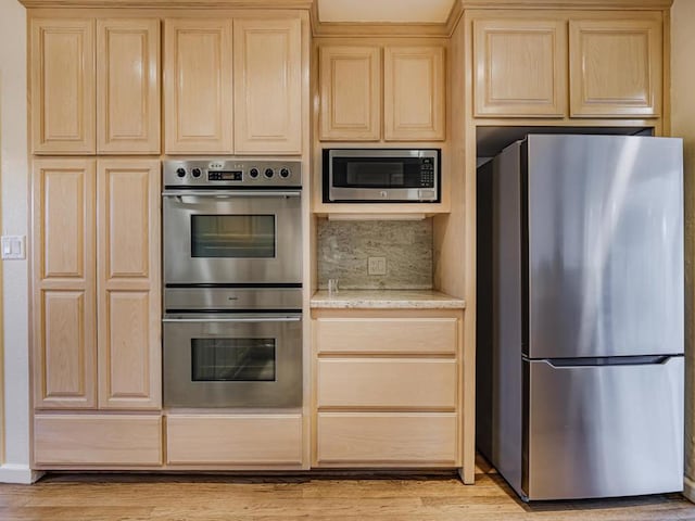 kitchen with stainless steel appliances, tasteful backsplash, light brown cabinetry, and light hardwood / wood-style flooring