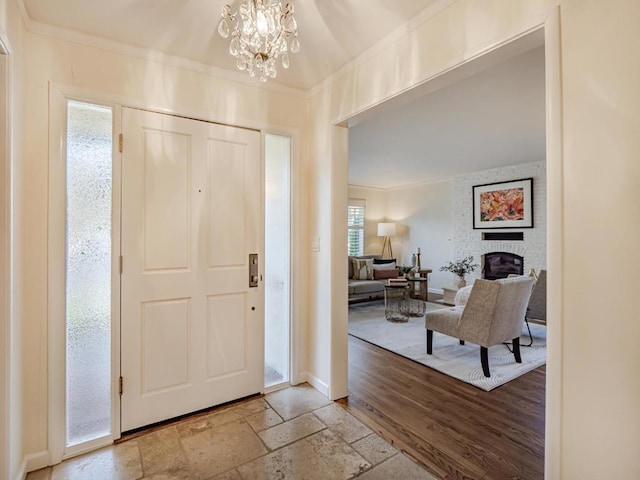 foyer entrance featuring crown molding, a large fireplace, light wood-type flooring, and a notable chandelier