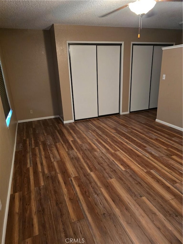 unfurnished bedroom with dark wood-type flooring, ceiling fan, multiple closets, and a textured ceiling