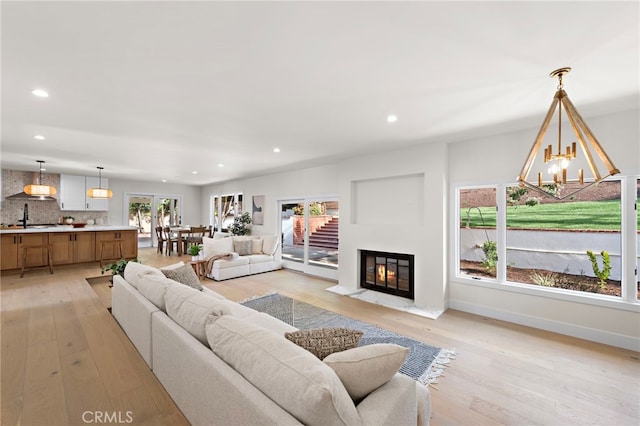 living room featuring an inviting chandelier, sink, and light hardwood / wood-style flooring