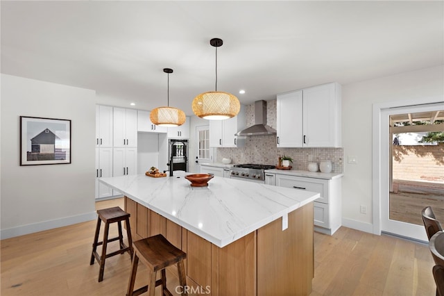 kitchen featuring white cabinetry, pendant lighting, a center island with sink, and wall chimney exhaust hood