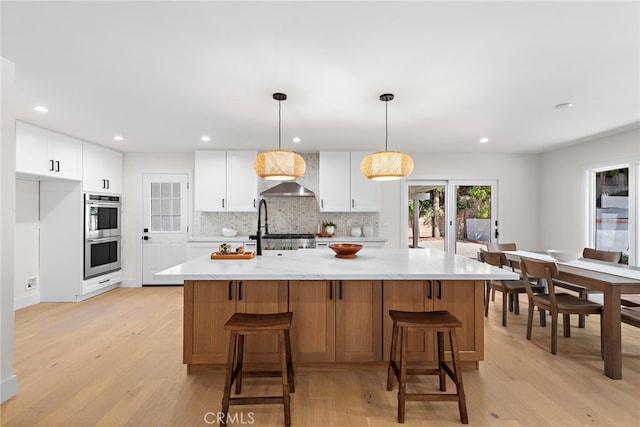 kitchen with white cabinetry, hanging light fixtures, and a center island with sink