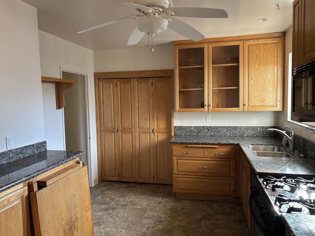 kitchen with gas stove, ceiling fan, dark stone counters, and sink