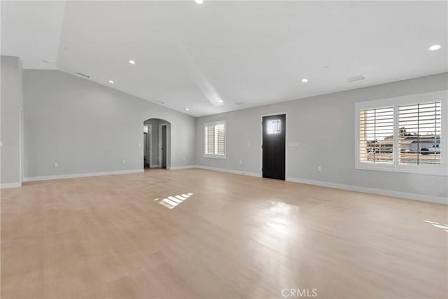 unfurnished living room featuring vaulted ceiling, a wealth of natural light, and light hardwood / wood-style flooring