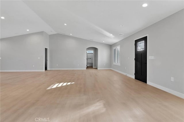 unfurnished living room with arched walkways, baseboards, vaulted ceiling, and light wood-type flooring