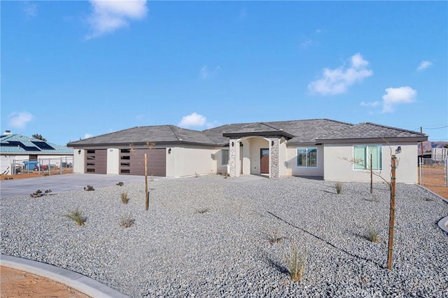 prairie-style house with fence, driveway, stucco siding, and a garage