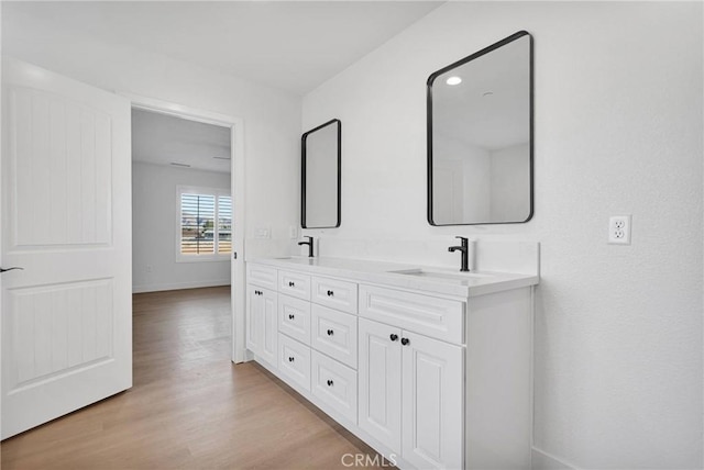 bathroom with a sink, double vanity, wood finished floors, and baseboards