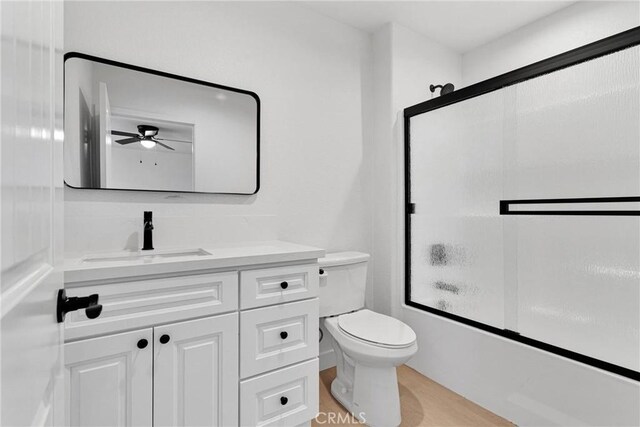 bathroom with bath / shower combo with glass door, toilet, wood finished floors, a ceiling fan, and vanity