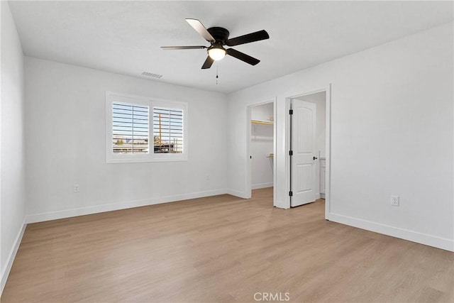 unfurnished bedroom with visible vents, baseboards, a ceiling fan, light wood-style floors, and a walk in closet