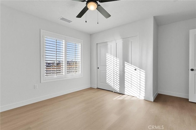 unfurnished bedroom with a closet, a ceiling fan, wood finished floors, baseboards, and visible vents