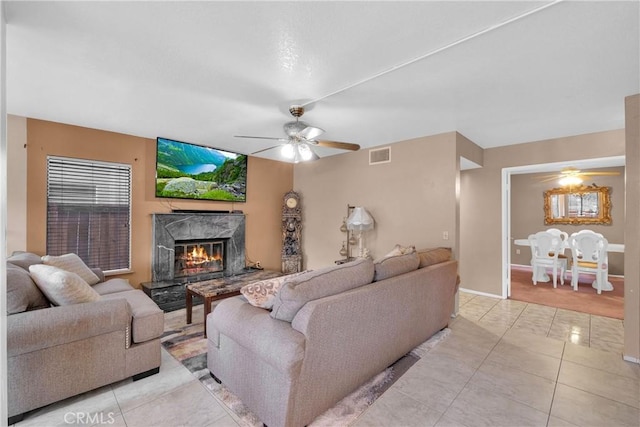 living room featuring light tile patterned floors, a premium fireplace, and ceiling fan