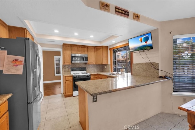 kitchen with sink, appliances with stainless steel finishes, a raised ceiling, decorative backsplash, and kitchen peninsula