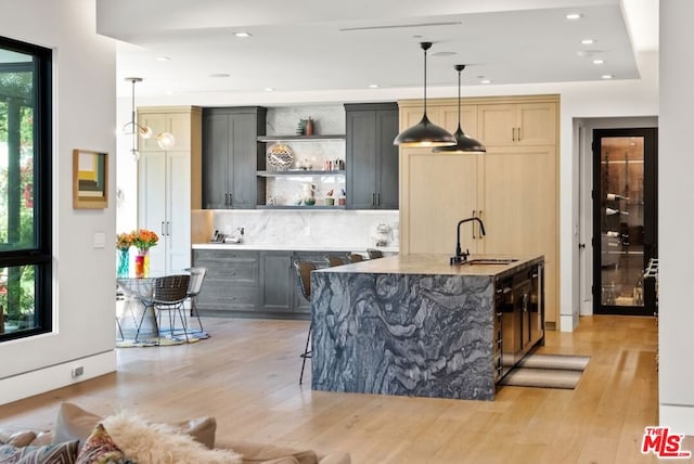 bar with light stone counters, decorative light fixtures, sink, and light hardwood / wood-style flooring