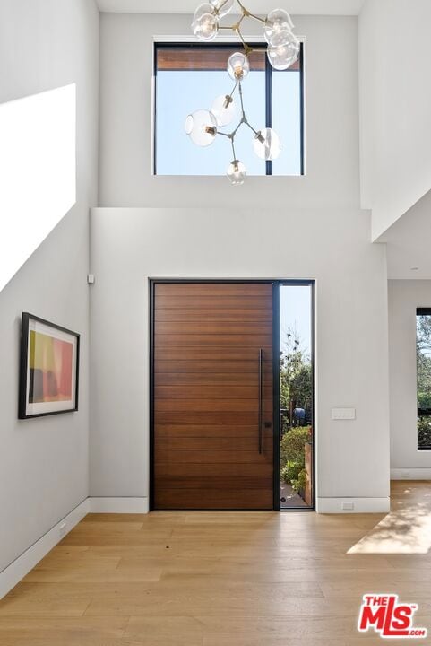 foyer entrance featuring a towering ceiling, an inviting chandelier, and light wood-type flooring