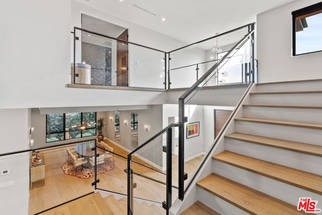 stairs with a towering ceiling, wood-type flooring, and plenty of natural light