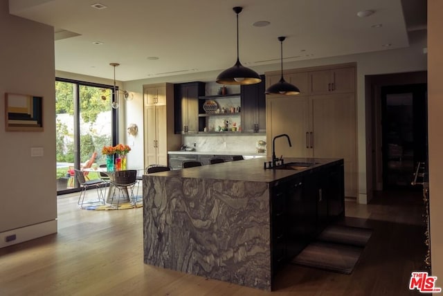 kitchen featuring sink, light hardwood / wood-style flooring, hanging light fixtures, tasteful backsplash, and a center island with sink