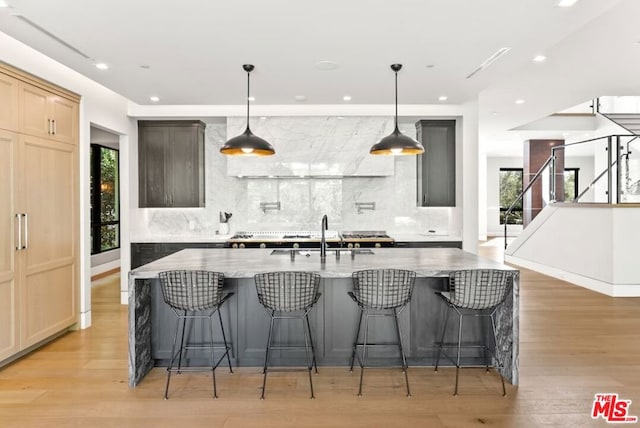 kitchen with sink, a spacious island, light stone countertops, decorative light fixtures, and light brown cabinets