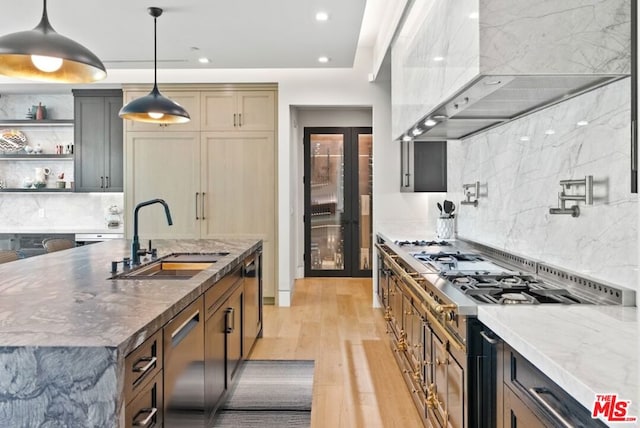 kitchen featuring sink, decorative light fixtures, a center island with sink, light hardwood / wood-style flooring, and dark stone counters