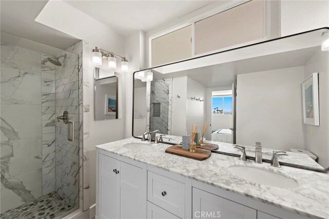 bathroom featuring a sink, a marble finish shower, and double vanity