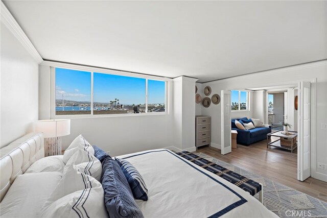 bedroom featuring wood finished floors, baseboards, a water view, and ornamental molding