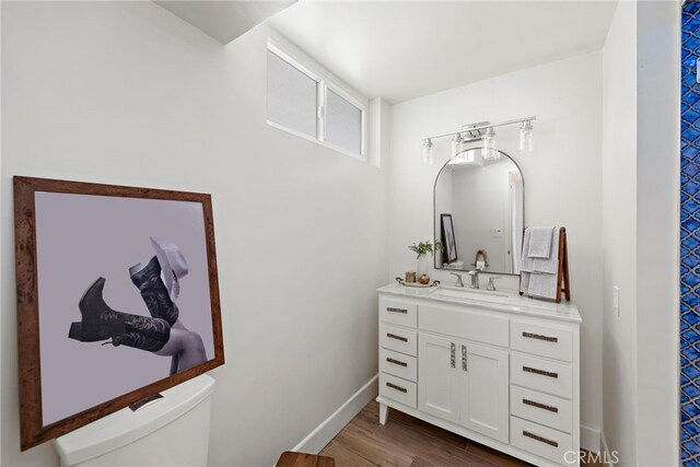 half bath with vanity, toilet, wood finished floors, and baseboards