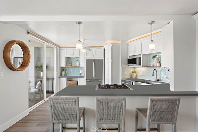 kitchen with dark countertops, appliances with stainless steel finishes, a peninsula, white cabinets, and open shelves