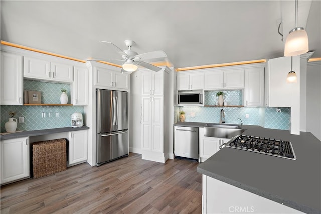 kitchen with dark countertops, wood finished floors, white cabinets, stainless steel appliances, and a sink