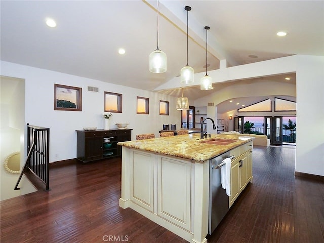 kitchen featuring lofted ceiling with beams, sink, hanging light fixtures, light stone counters, and a center island with sink