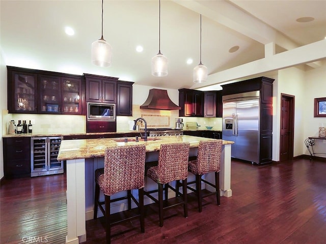 kitchen featuring premium range hood, wine cooler, light stone counters, built in appliances, and hanging light fixtures