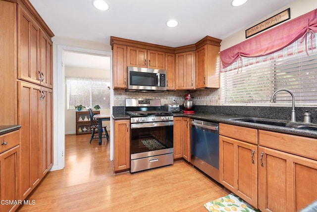 kitchen featuring sink, appliances with stainless steel finishes, dark stone countertops, light hardwood / wood-style floors, and decorative backsplash