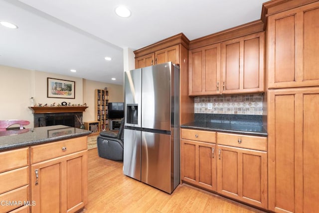 kitchen with tasteful backsplash, stainless steel refrigerator with ice dispenser, light hardwood / wood-style floors, and dark stone counters