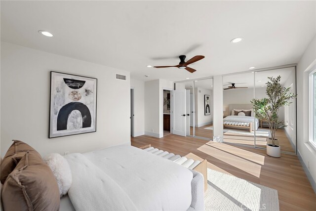 bedroom featuring ceiling fan, light hardwood / wood-style flooring, and two closets