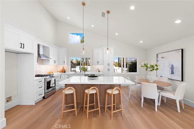 kitchen with white cabinetry, gas stove, a kitchen island, decorative light fixtures, and wall chimney exhaust hood